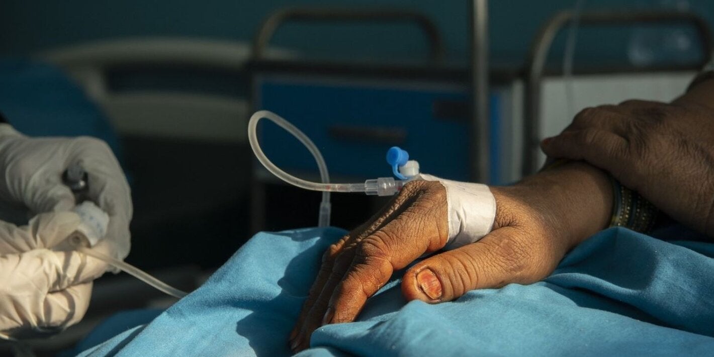 photo of a hand of a patient with an IV and two hands of a health worker adjusting it