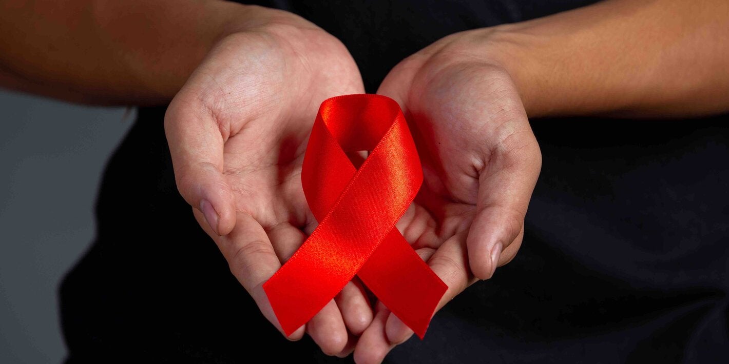 Manos sosteniendo listón rojo refernte al VIH/SIDA