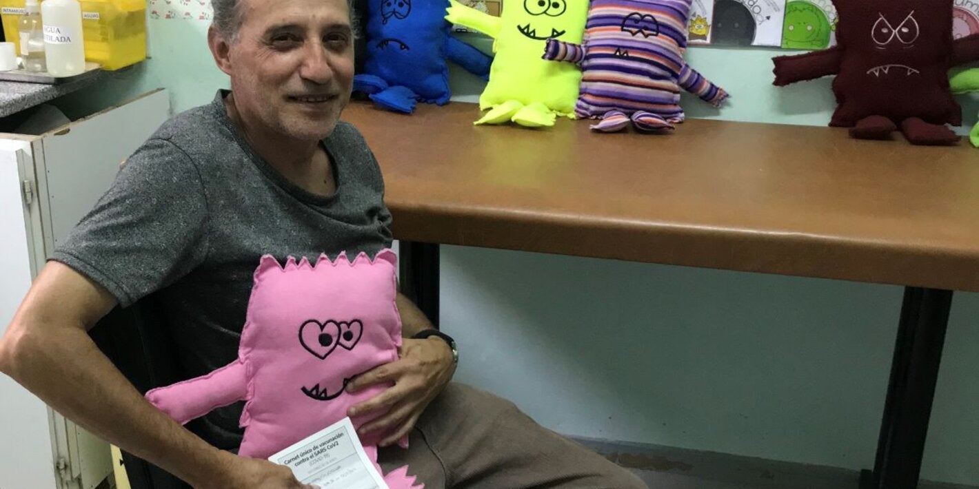 Foto de un hombre que acaba de recibir la vacuna y tiene entre sus brazos el muñeco de la alegría que expresa su sentimiento en torno a la vacunación