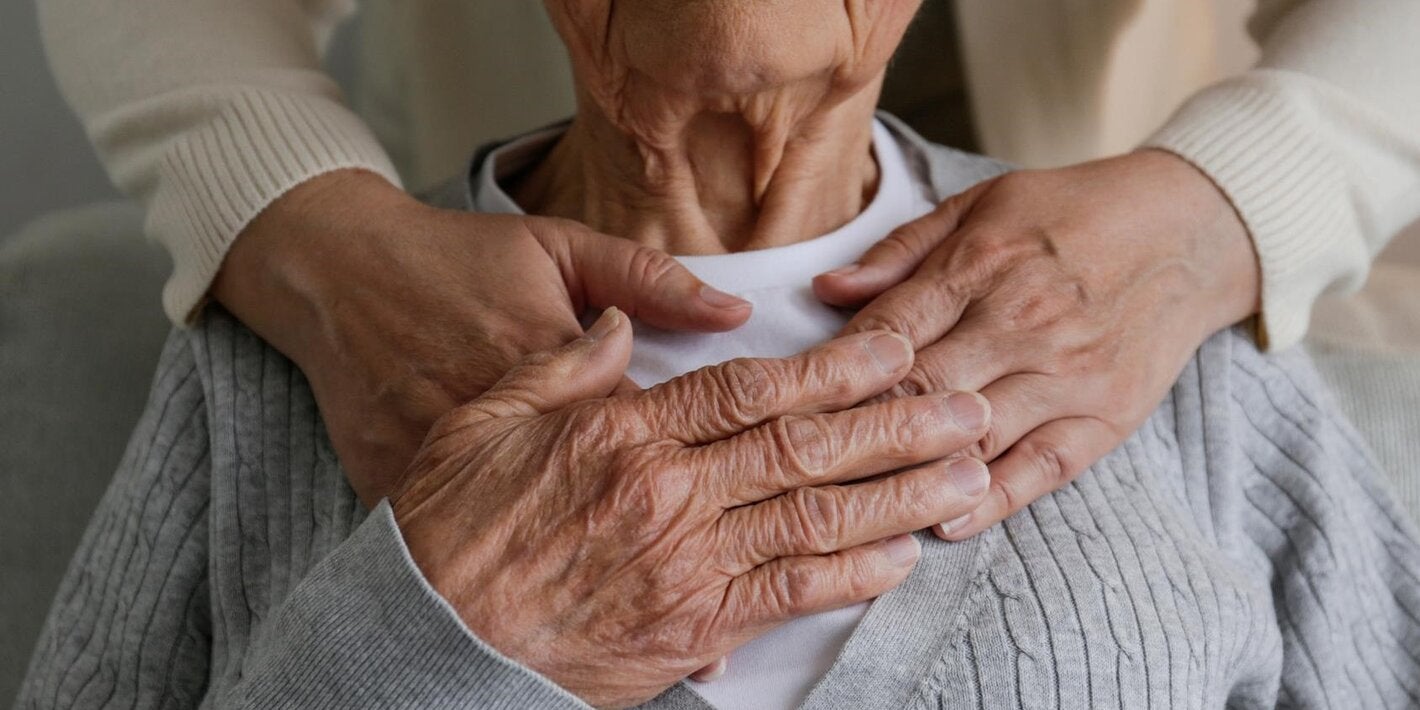 Old woman embraced by hands of another person from her back