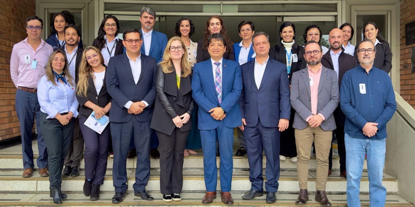 Participantes del evento (hombres y mujeres) con ropa ejecutiva, posan en las escaleras de la entrada de un edificio.