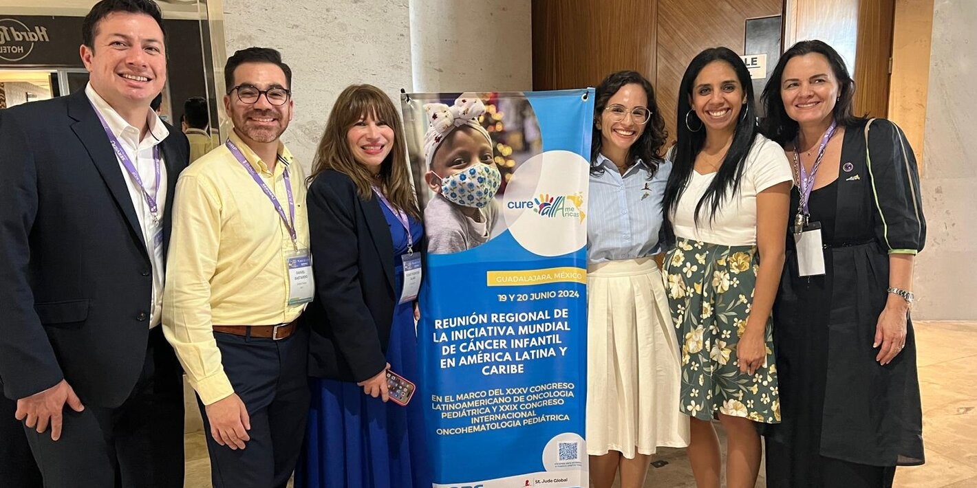 Fotografía de varias personas junto al banner que anuncia la reunión regional de CureAll Americas