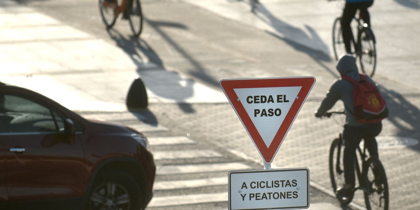 Foto de una calle con ciclistas, un cartel de ceda el paso y un auto esperando