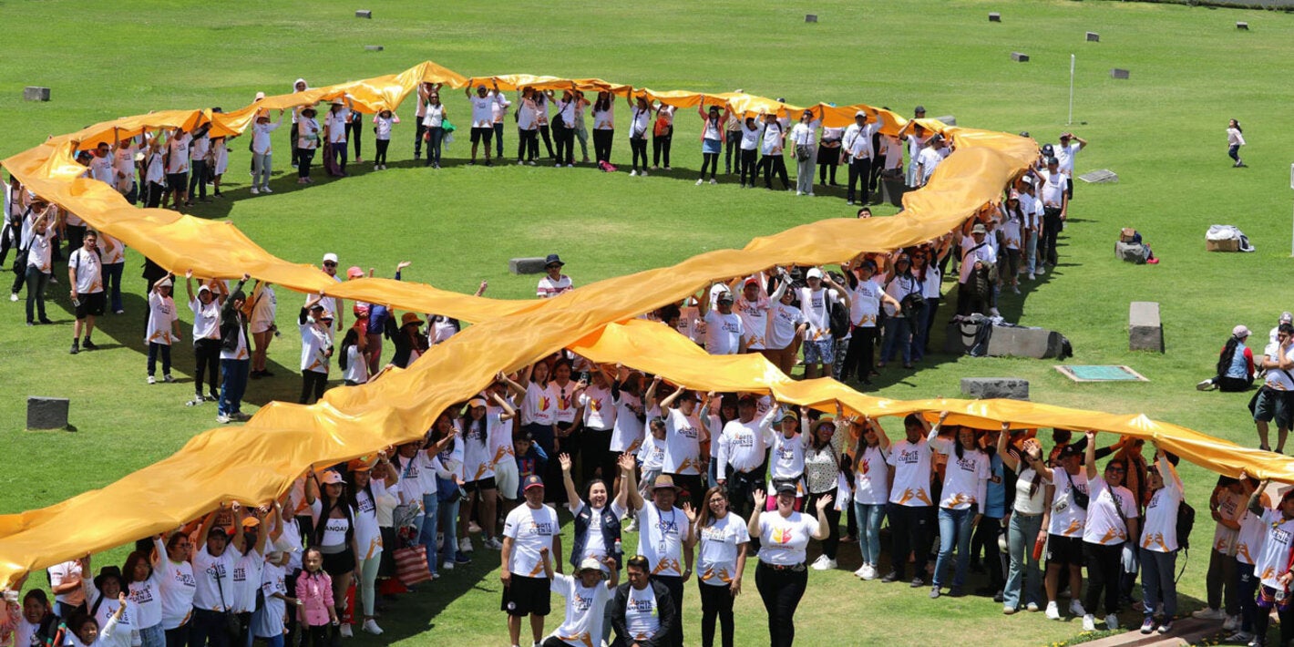 Personas en un campo amplio sosteniendo el emblema del cáncer infantil (lazo dorado)