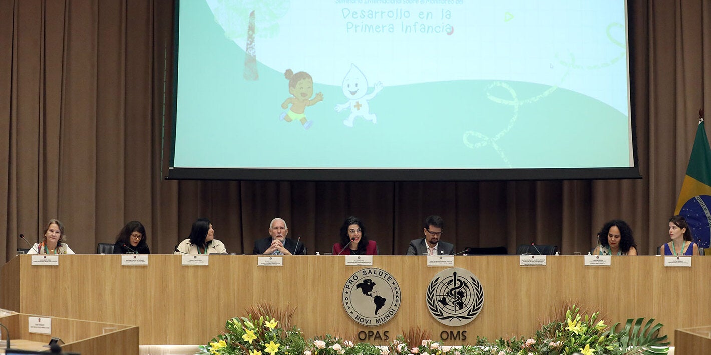 Mesa de abertura do evento com oito pessoas e um telão ao fundo escrito "Desenvolvimento na primeira infância"