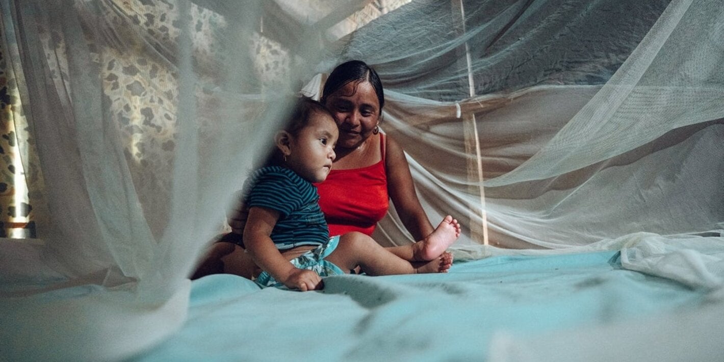 Mother and child under mosquito net over bed