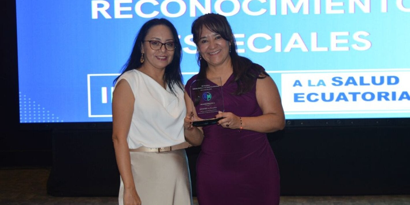 La representante de la OPS/OMS en Ecuador, Dra. Sonia Quezada, recibe de la periodista Cristina Coello, el reconocimiento entregado a la oficina de parte de Edición Médica.