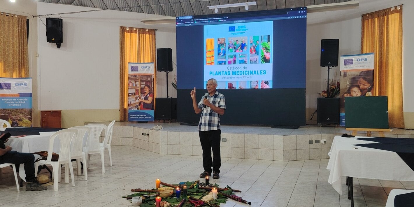Un hombre frente a una pantalla luminosa, presenta el catálogo de plantas medicinales del pueblo maya Ch'orti'