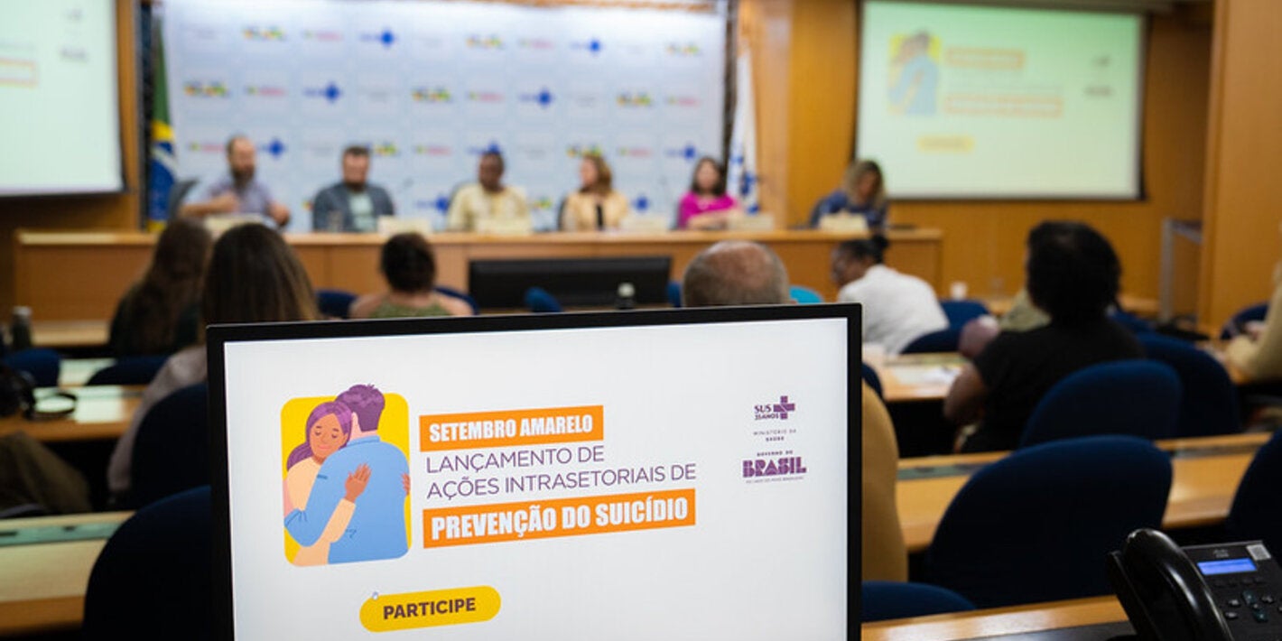 logomarca do evento, ao fundo mesa de palestrantes