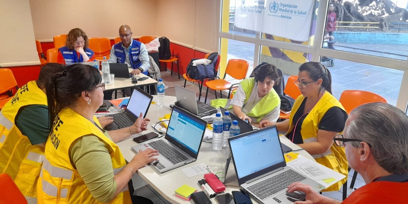 participantes de taller con chalecos amarillos, sentados alrededor de una mesa con laptops