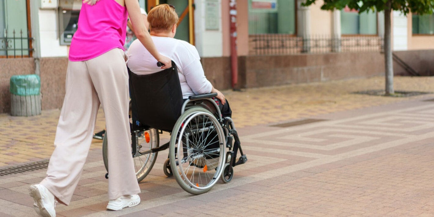 Mujer joven empuja a una mujer mayor en silla de ruedas