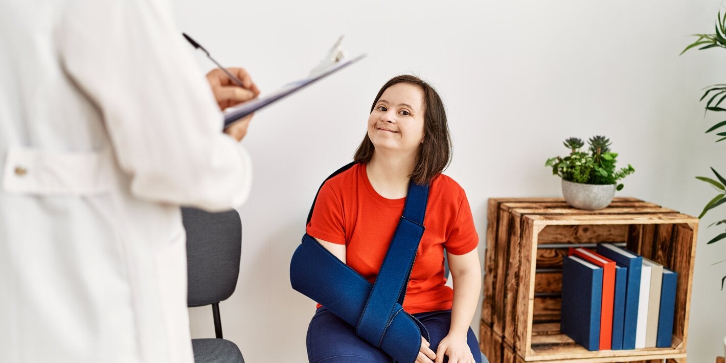 Brunette woman with Down syndrome sitting with her arm in a sling in the waiting room