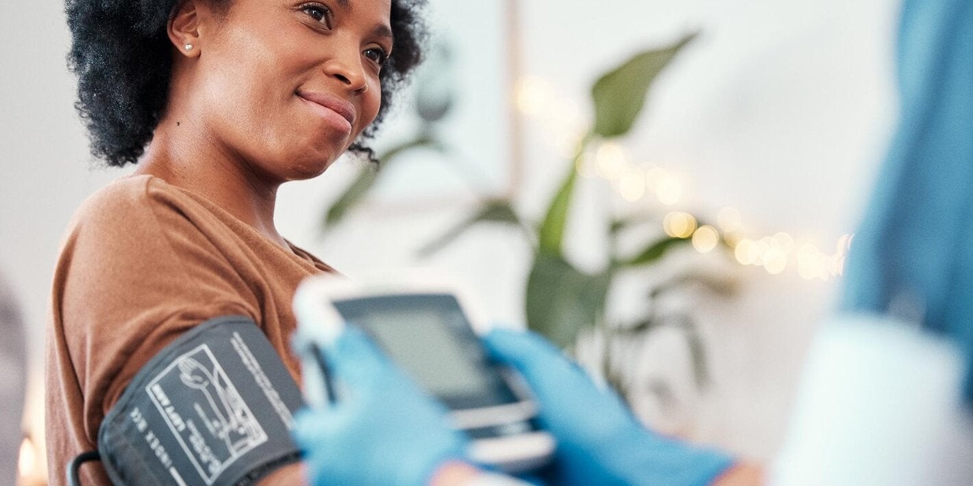 Healthcare personnel are taking the blood pressure of a young African-American woman using an automatic device.