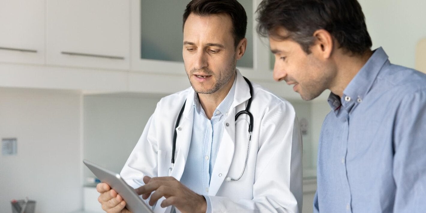 Un médico de atención primaria muestra una tablet a un paciente vestido con camisa azul