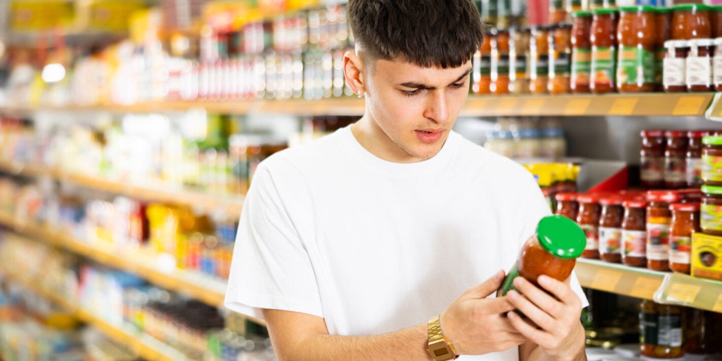 A young man reading the front label of the product (sauce).