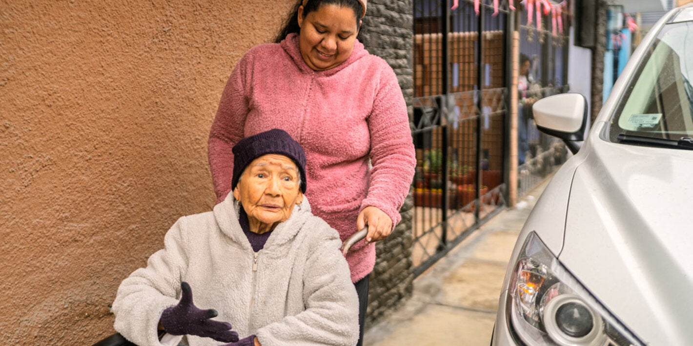 eldely woman in wheelchair being pushed by femaile care worker