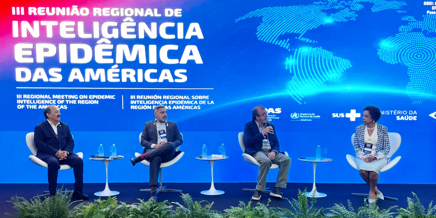 Panelistas sentados con fondo alusivo al evento, mostrando mapa mundi y título del evento