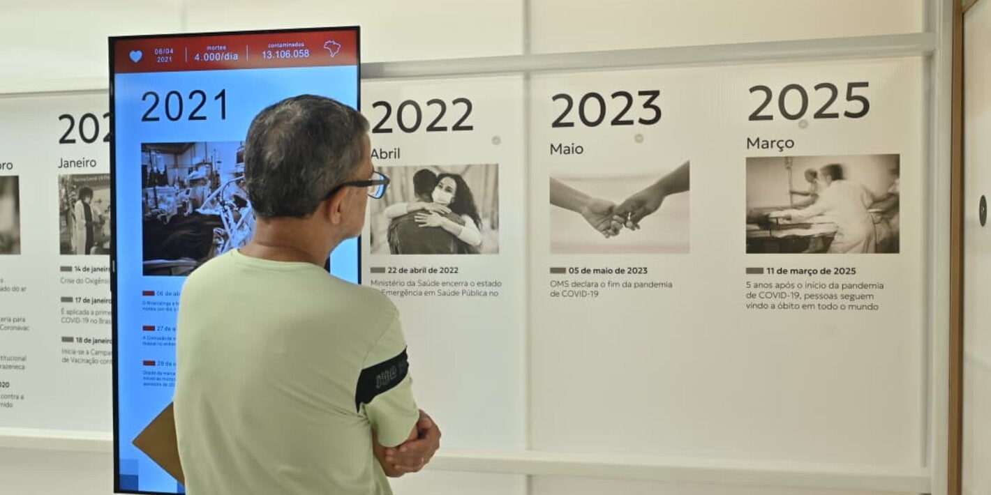 Un visitante observa una instalación interactiva con una línea de tiempo en la exposición “La memoria infinita de la pandemia. La historia de la COVID-19 por todos nosotros, los brasileños”, concebida como una extensión física del Memorial Digital para acercar a la sociedad a las historias y experiencias preservadas en el Portal.