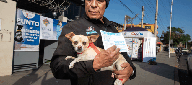 ""hombre sosteniendo un perro recién vacunado con la cartilla de vacunación en mano