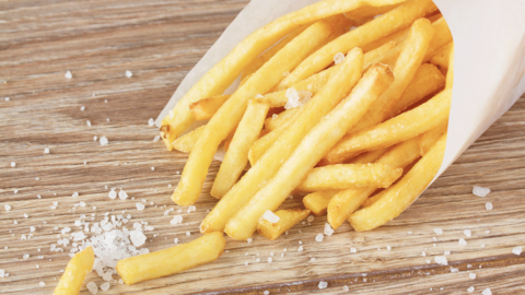 French fries in a white bag on a brown countertop with salt grains scattered 
