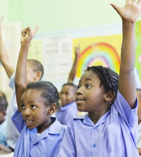Primary school children in a classroom raising hands to answer a question