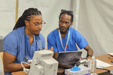 Two male nurses in scrubs discussing results before a laptop