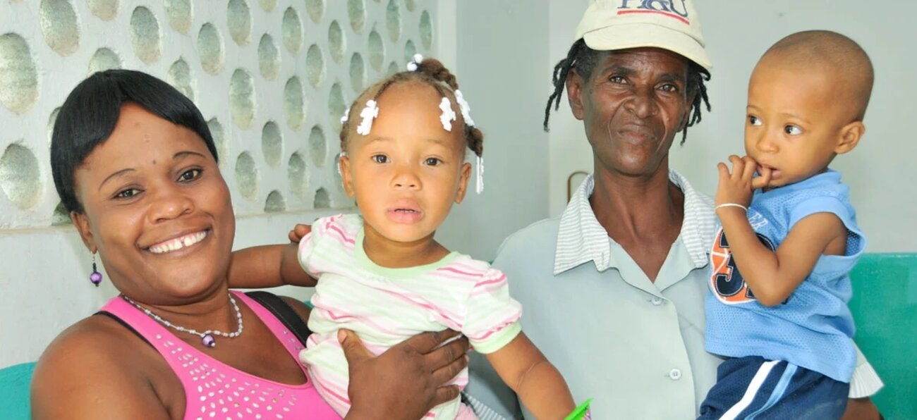 Family — the mother is seen carrying a young girl, while a man beside her is holding another child