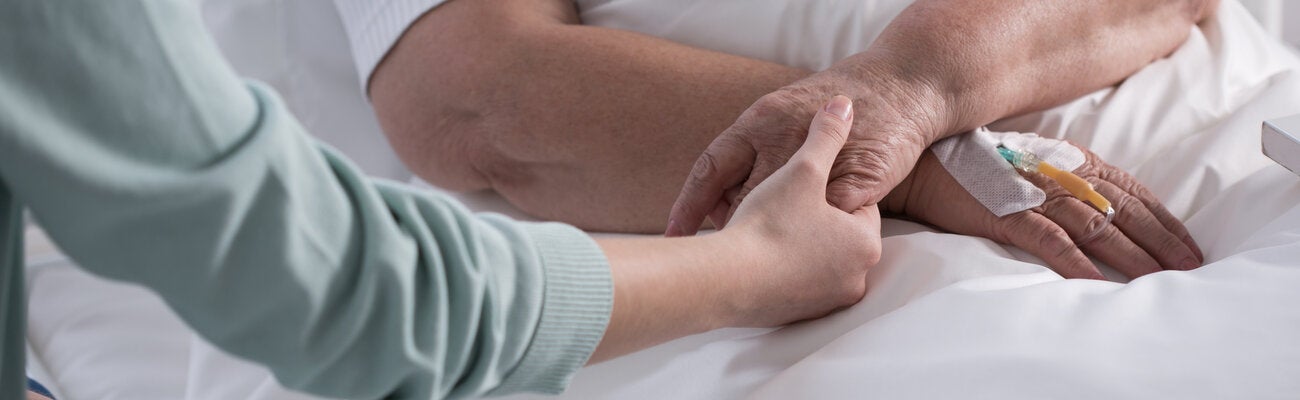Mano de trabajador de salud sosteniendo las dos manos de una persona acostada en una cama de hospital