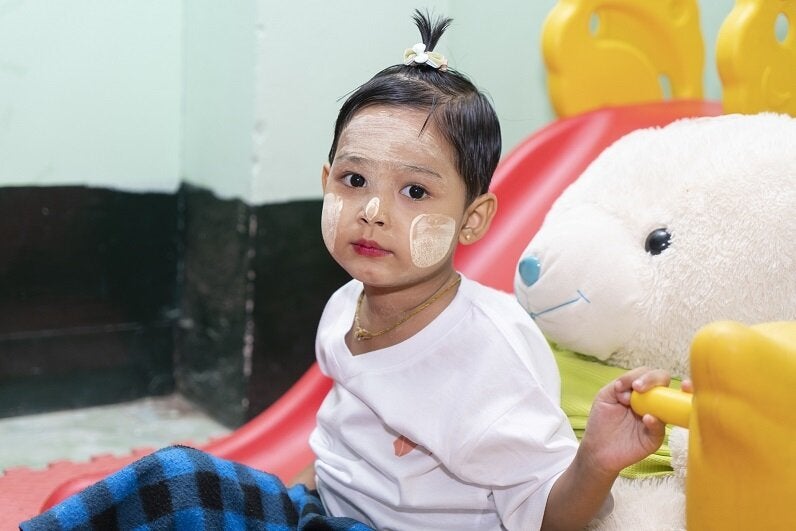 Foto de una niña pequeña con pintura en su rostro y sentada junto a un conejito de peluche gigante