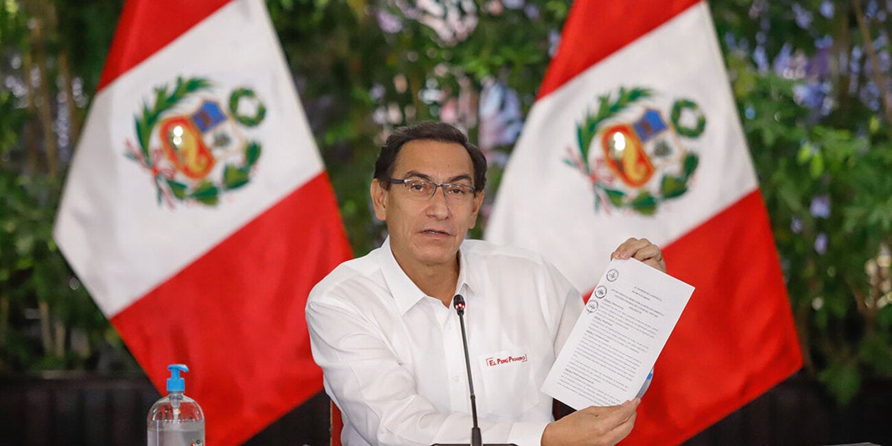 El ex presidente de Perú, Martín Vizcarra, muestra un documento en papel con el texto de la ley de cáncer infantil, flanqueado por dos banderas de Perú al fondo