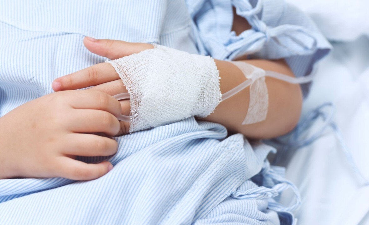 Foto de las manos de un niño hospitalizado, con la mano izquierda vendada y con una vía