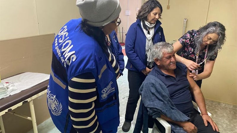 Elderly man being vaccinated by health worker and PAHO staff