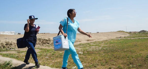 Health care worker walking throught the mountains of Peru with vaccination equipment