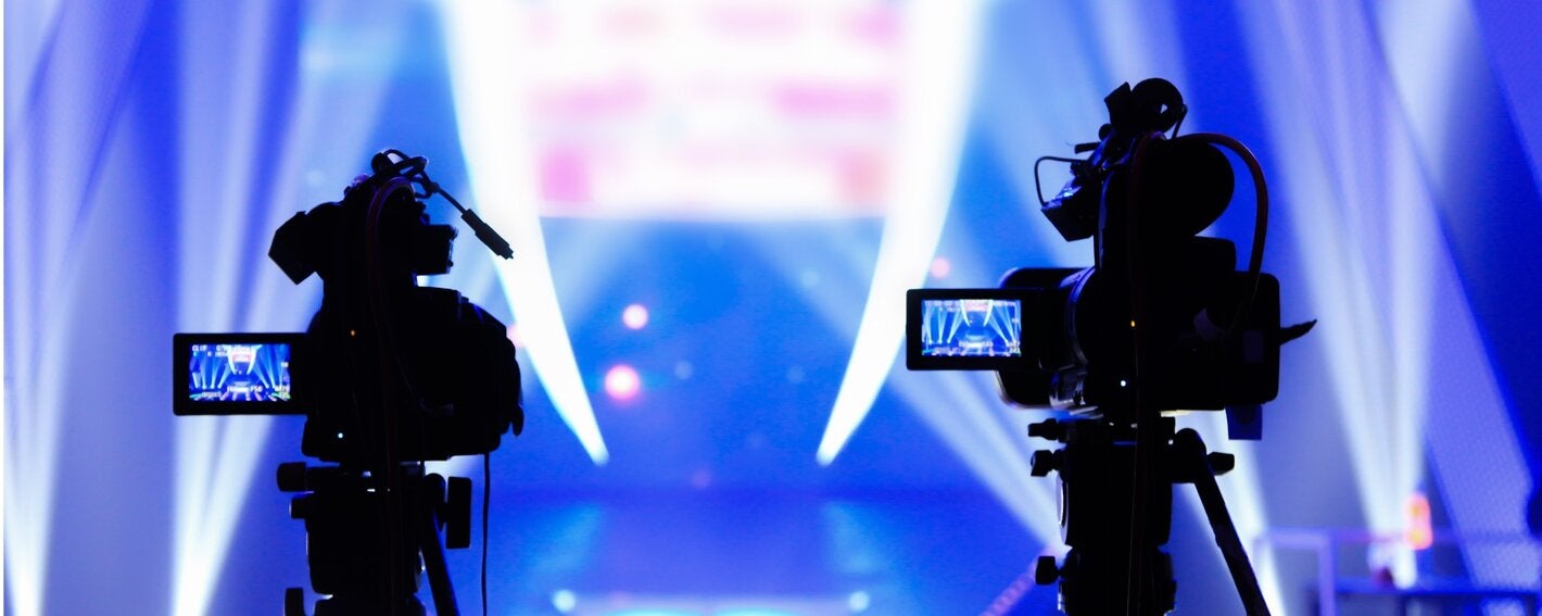 silueta de dos cámaras grabando un escenario con luces