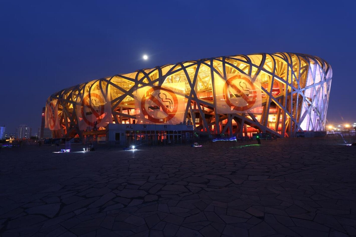 Photo of a big building shaped as a elipse, with no walls, shape made of the bent beams. In the exterior, four large banners with the icon of prohibited smoking