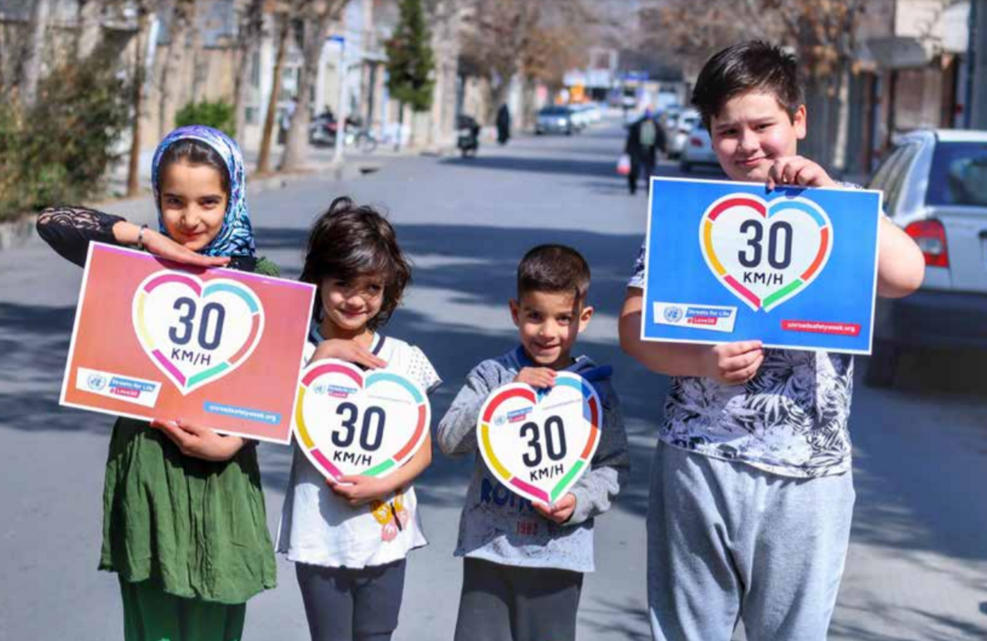 Foto de cuatro niños en medio de una calle sin tráfico sosteniendo carteles con el dibujo de un 30 dentro de la silueta de un corazón