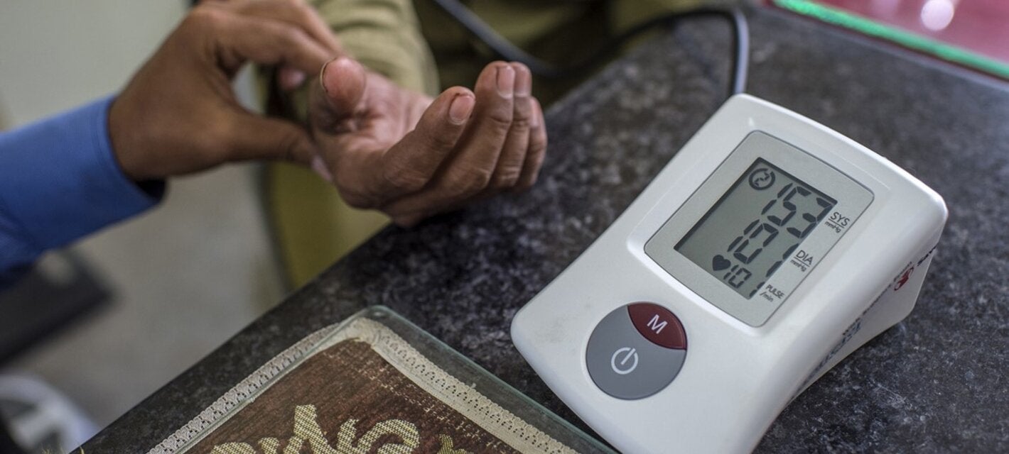 Close up of a glucometer and in the back a hand holding the hand of a patient