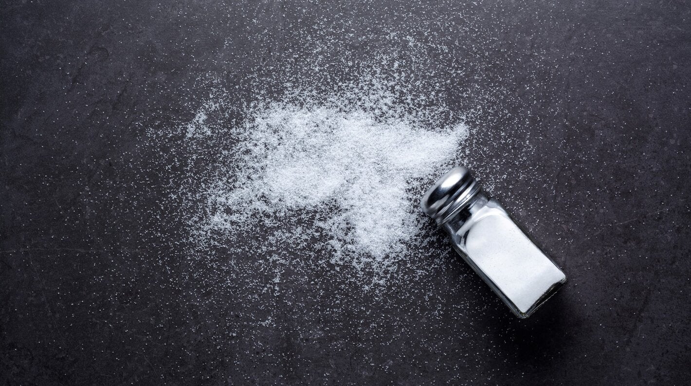 Salt shaker with salt spilt around on a dark background
