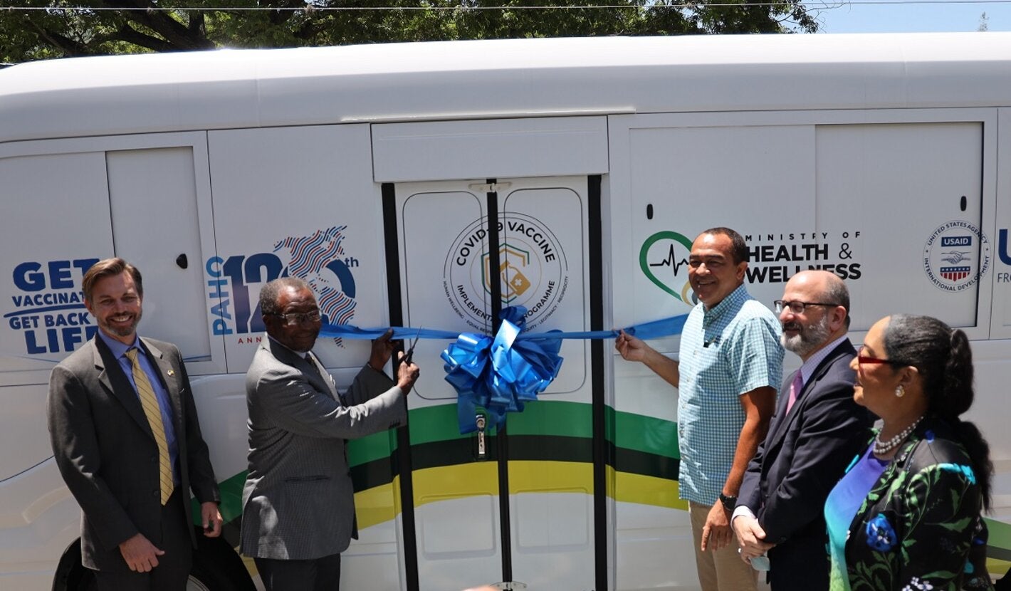 US Ambassador Mr. Nick Perry (2nd right) and Dr. the Honourable Christopher Tufton, Minister of Health and Wellness (3rd right) are ready to cut the ribbon for the newly donated mobile vaccination unit. In good spirits and smiling are (L-R) Mr. Alex Gainer, Acting Country Representative for USAID in Jamaica, Mr. Ian Stein, PAHO/WHO Representative to Jamaica, Bermuda and the Cayman Islands and Dr. Marion Bullock DuCasse, Advisor for Health Emergencies at PAHO.