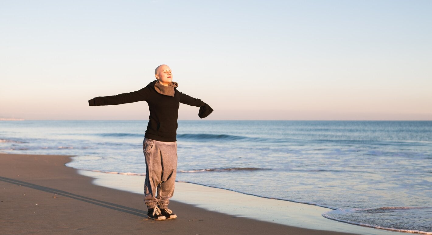 Bald woman with her arms extended in cross, breathing in in a beach.