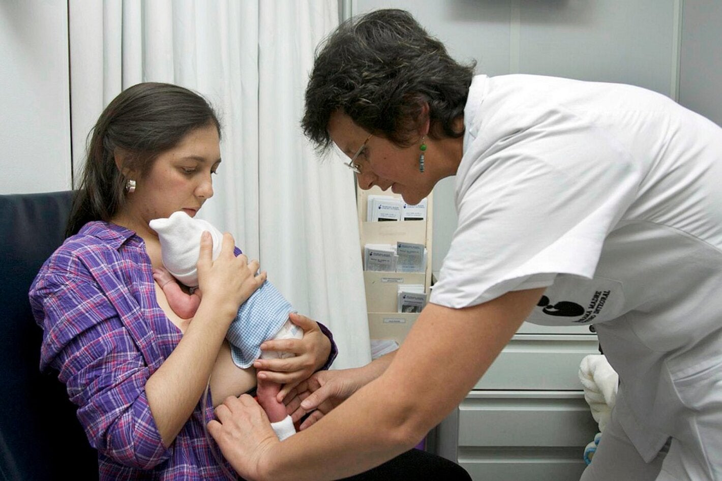 Madre con bebé en el pecho y enfermera ayudando
