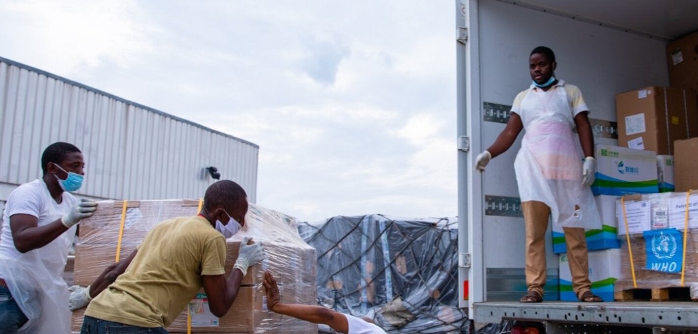 Photo of a group of workers pulling up a load of medicines marked with WHO logo into a truck