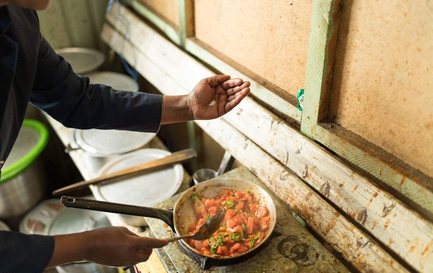 A person is adding salt to food as it cooks