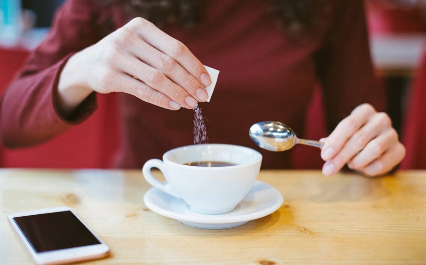 Person adding sugar to beverage. Avoid non-sugar sweeteners