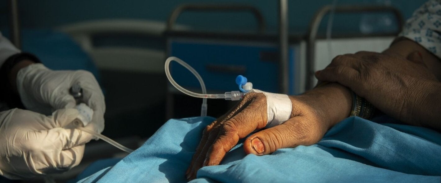 photo of a hand of a patient with an IV and two hands of a health worker adjusting it