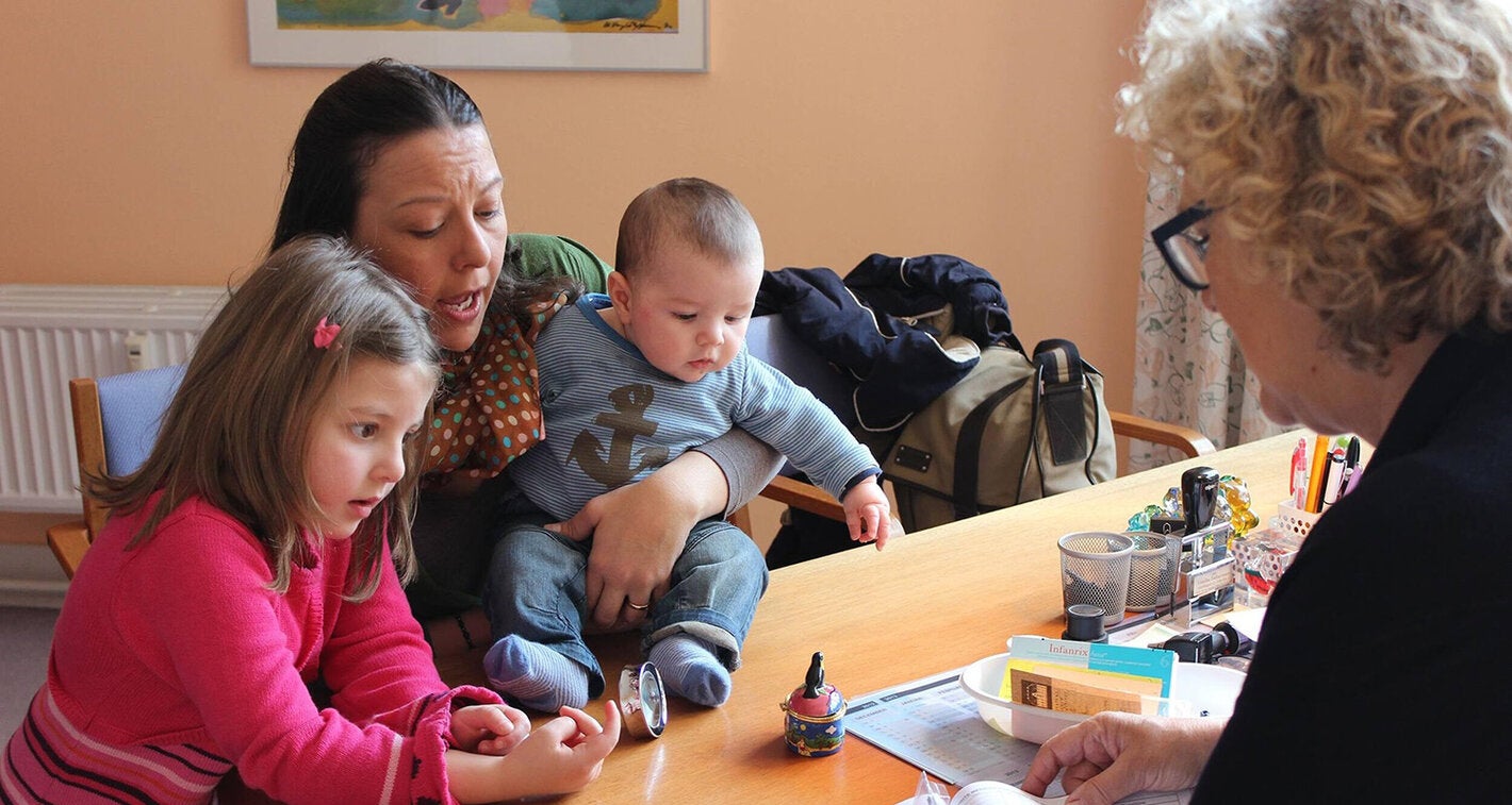 A doctor explaining vaccination procedures to a mother with her two young children.