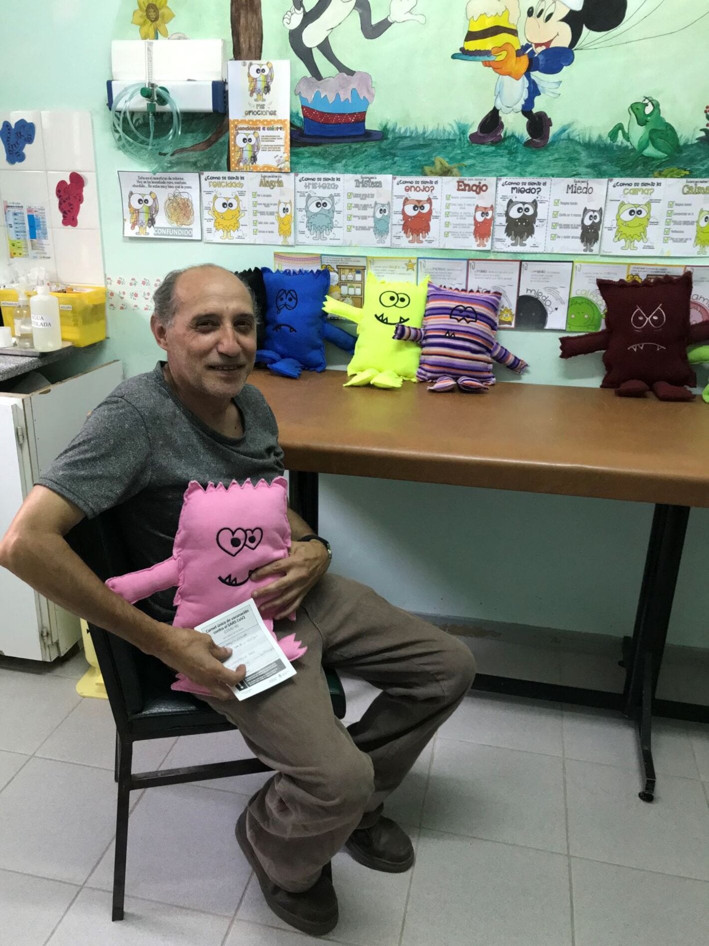 Foto de un hombre que acaba de recibir la vacuna y tiene entre sus brazos el muñeco de la alegría que expresa su sentimiento en torno a la vacunación