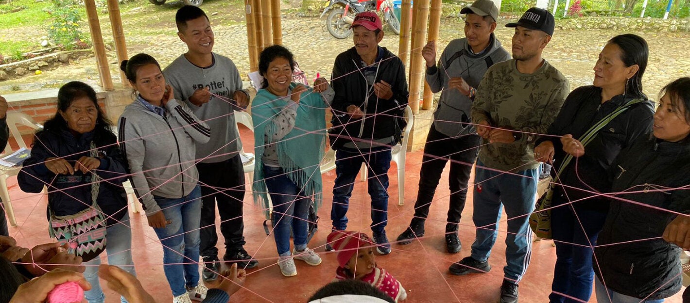 Indigenous people forming a circle and grabing a thin red interconected rope