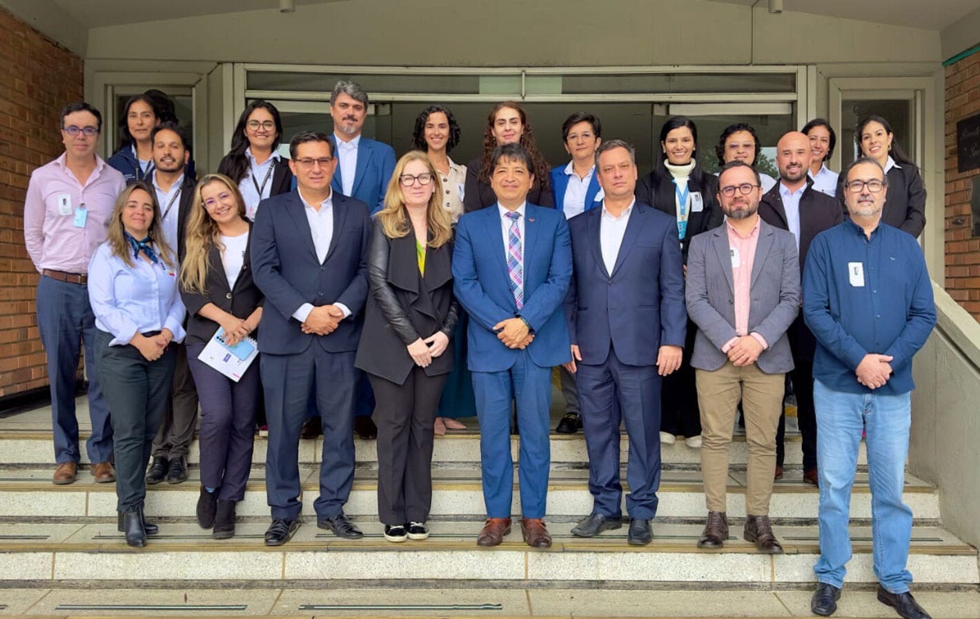 Participantes del evento (hombres y mujeres) con ropa ejecutiva, posan en las escaleras de la entrada de un edificio.