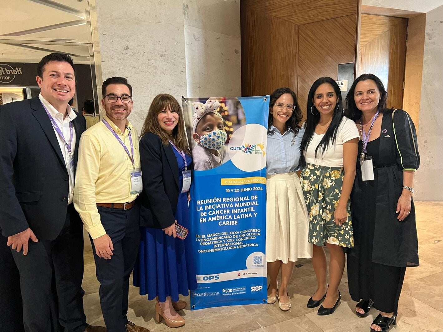 Fotografía de varias personas junto al banner que anuncia la reunión regional de CureAll Americas